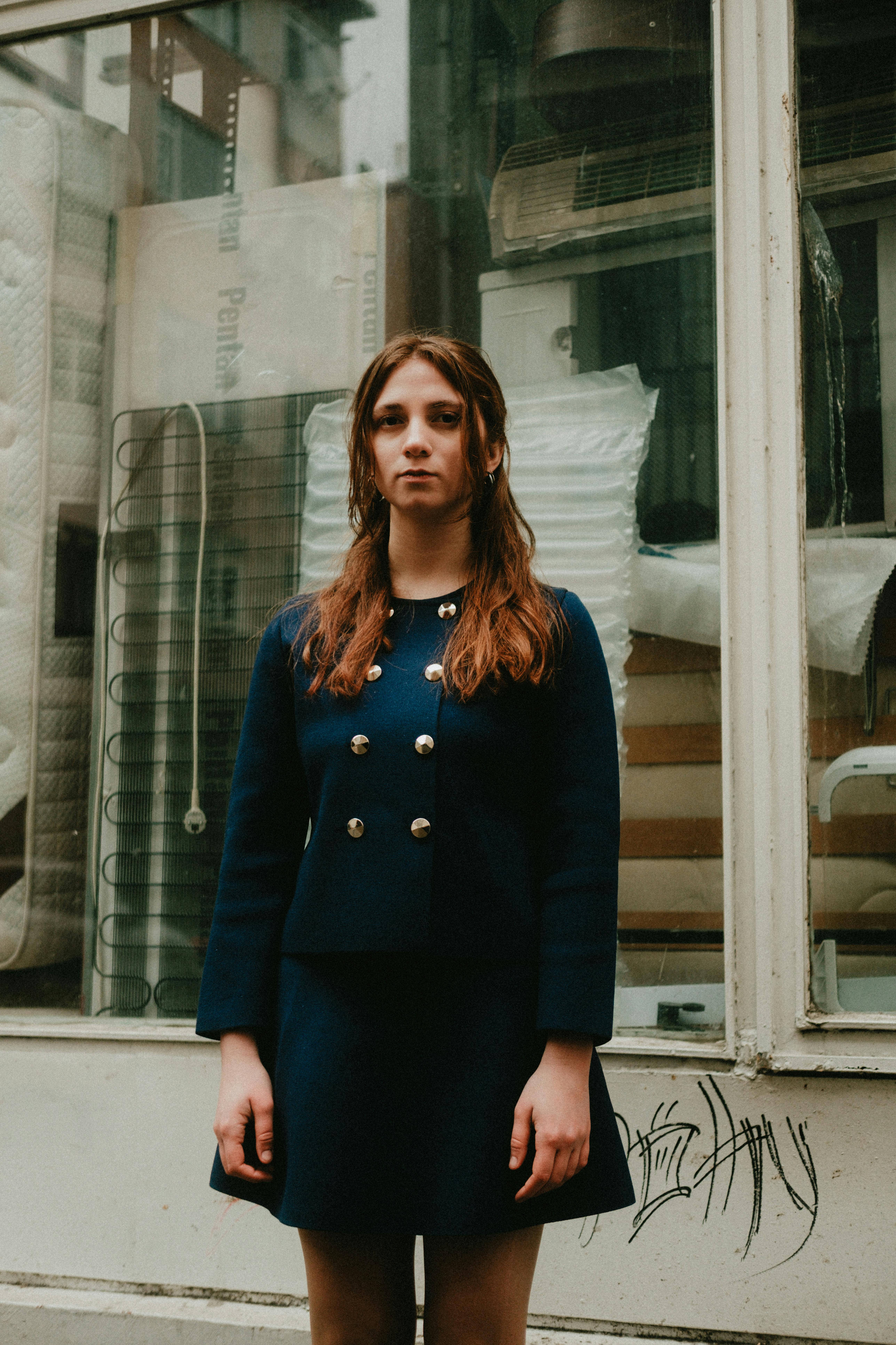 Woman in a blue coat stands confidently outside a mattress store. Urban setting.