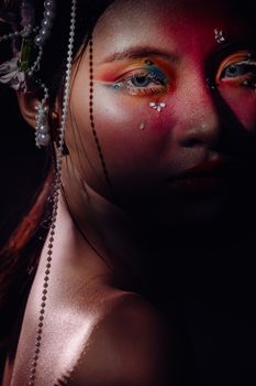 Moody portrait showcasing artistic makeup and intricate jewelry under dramatic lighting.