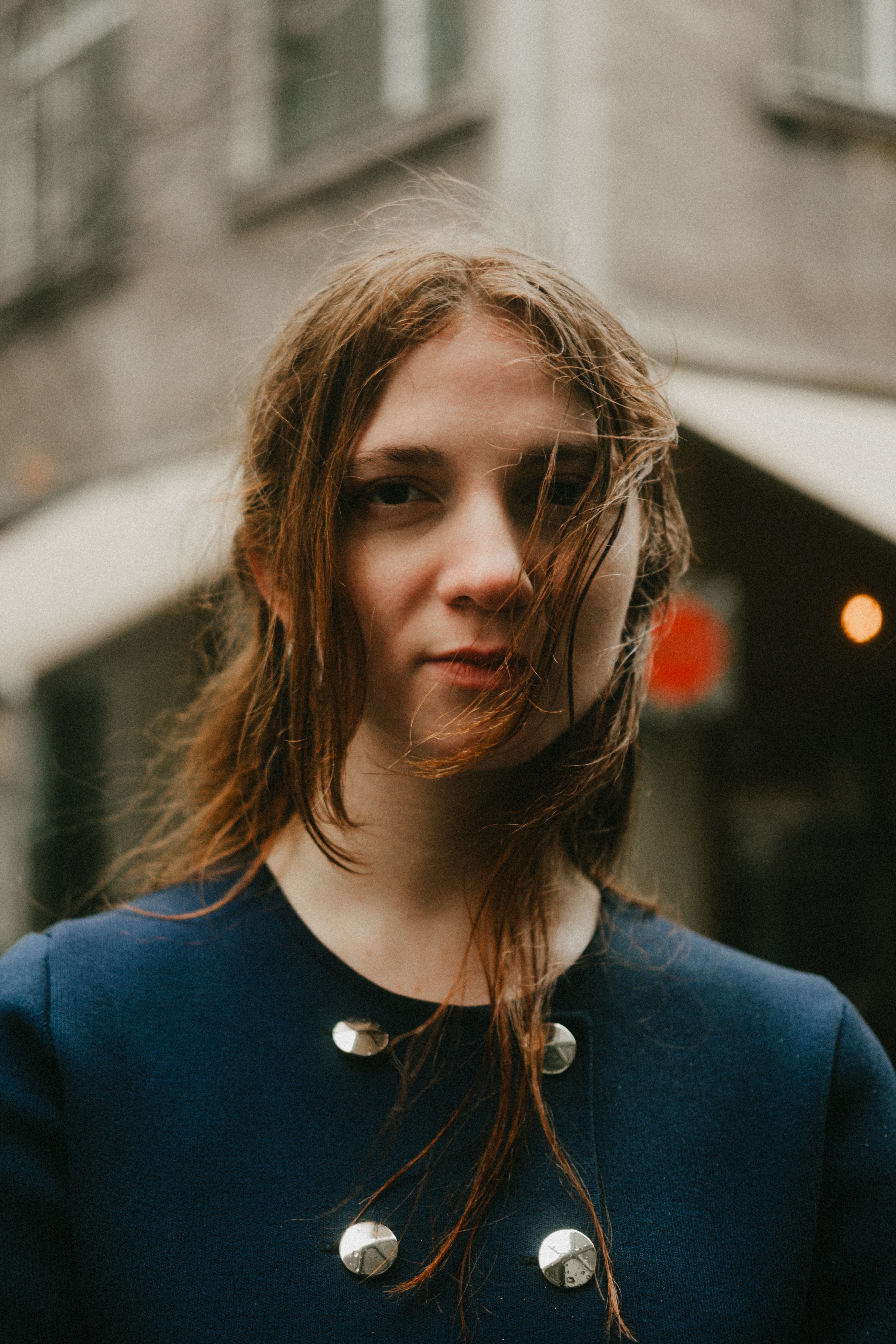 Young woman with long hair in a blue coat, moody urban setting.