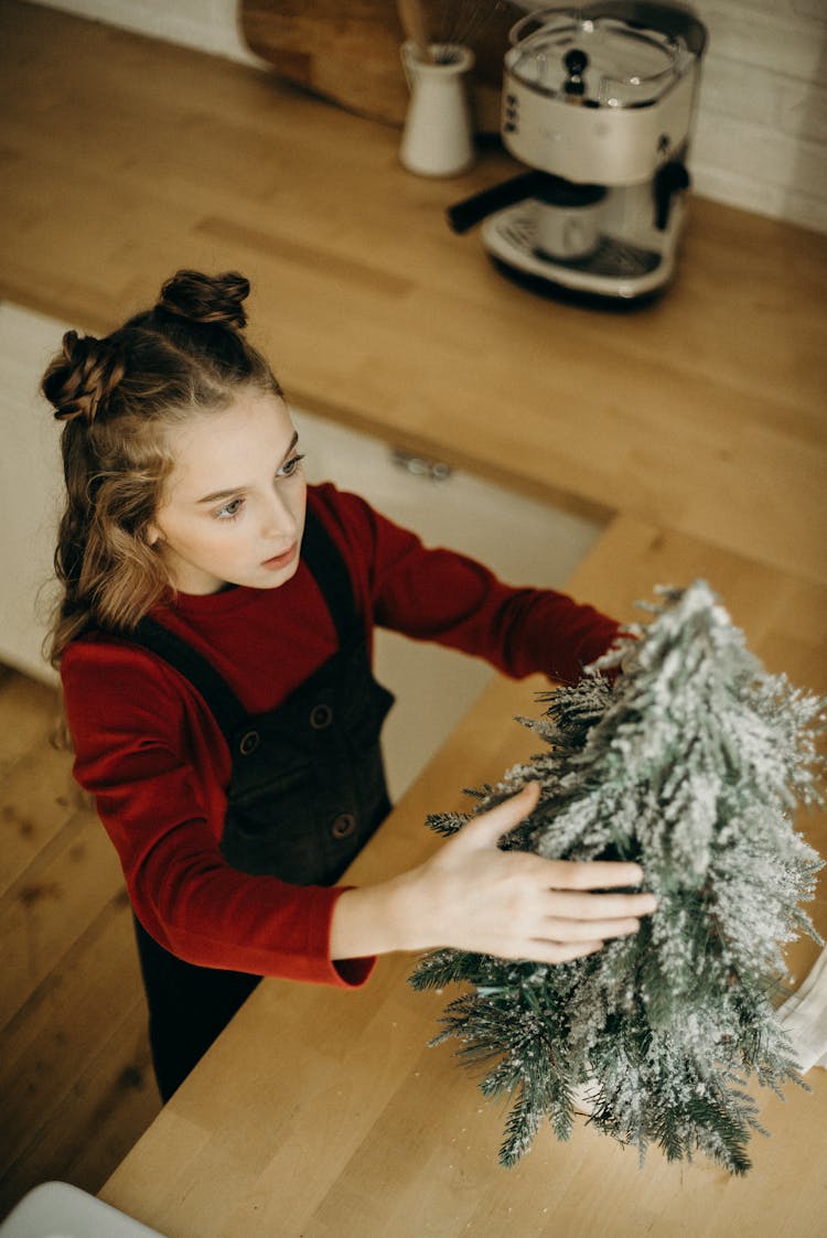 Girl Putting A Christmas Tree Decoration On Counter Top