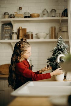 一个女孩在厨房的柜台上装饰一棵小圣诞树，室内布置得很温馨