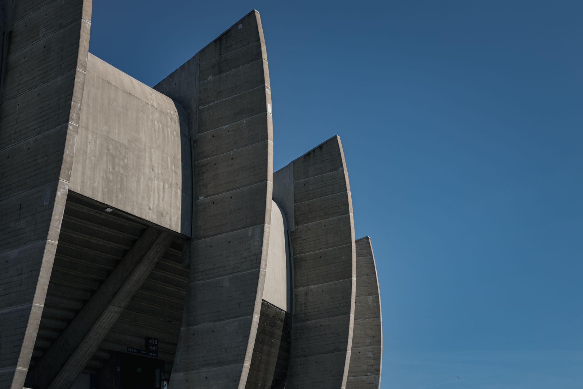 A striking modern architectural structure made of concrete photographed against a clear blue sky.