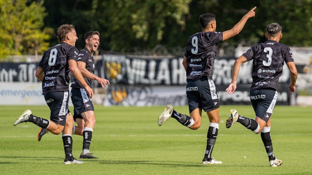 Soccer players in black uniforms celebrate a goal on a sunny outdoor field, capturing the essence of teamwork and victory.