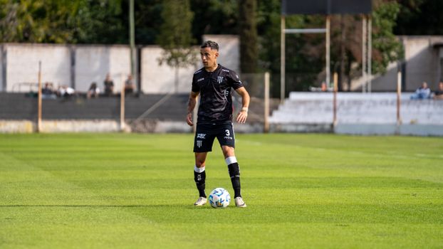 A focused soccer player in black uniform holding the ball on a sunny day match.