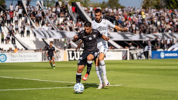 Two soccer players in action during a competitive outdoor match with a cheering crowd.