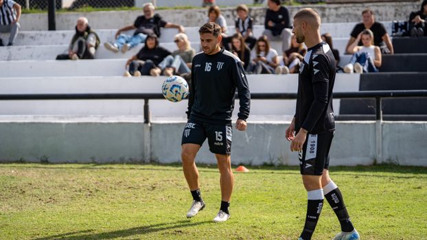 Soccer players training outdoors with spectators watching on a sunny day.