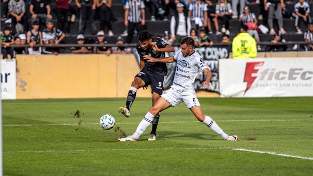 Intense soccer match moment with two players competing for the ball during day game.
