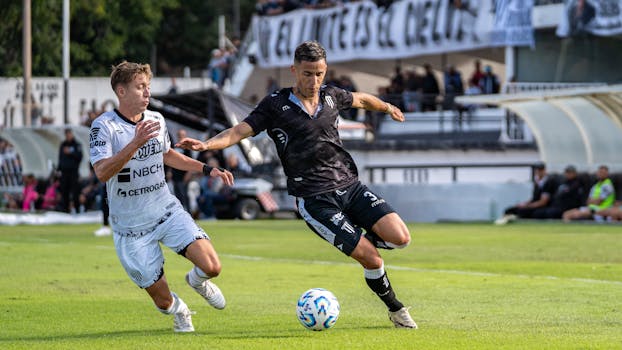 Two players compete intensely in an outdoor soccer match on a bright day.