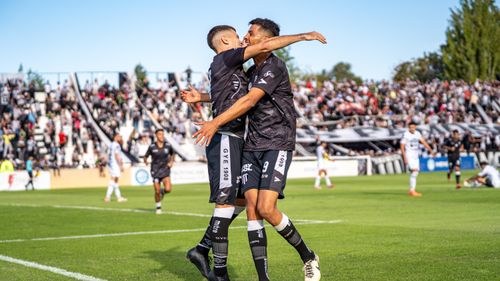 Free Two soccer players in black jerseys celebrate a goal on a sunny day at a packed stadium. Stock Photo