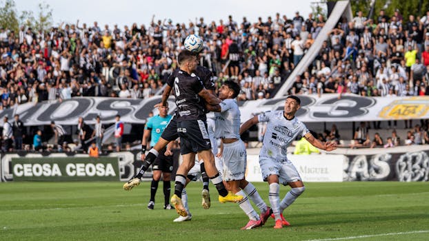 Soccer players in action during a competitive match with a lively crowd in the background.