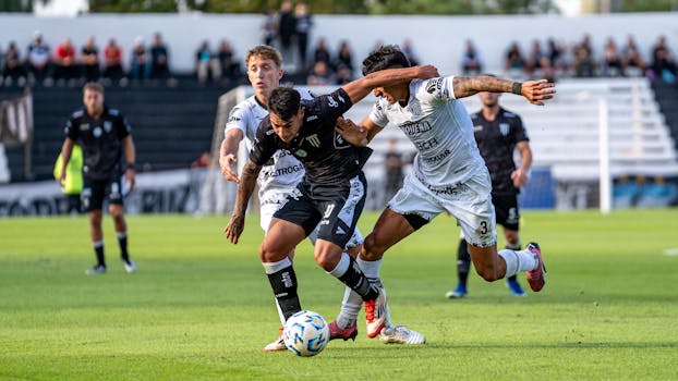 Dynamic action shot of two soccer players competing on a bright green field during the day.