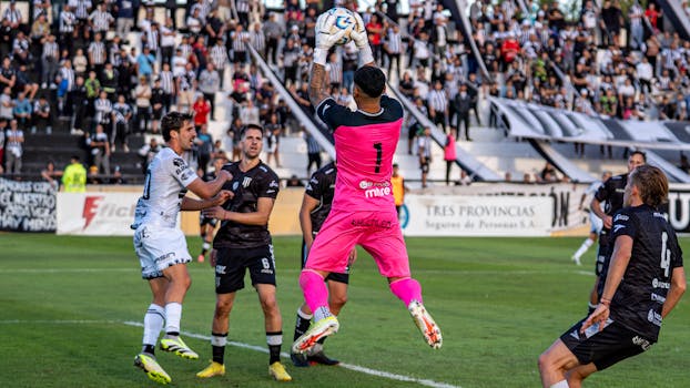 Soccer game scene with goalkeeper catching the ball in bright pink kit during a match.