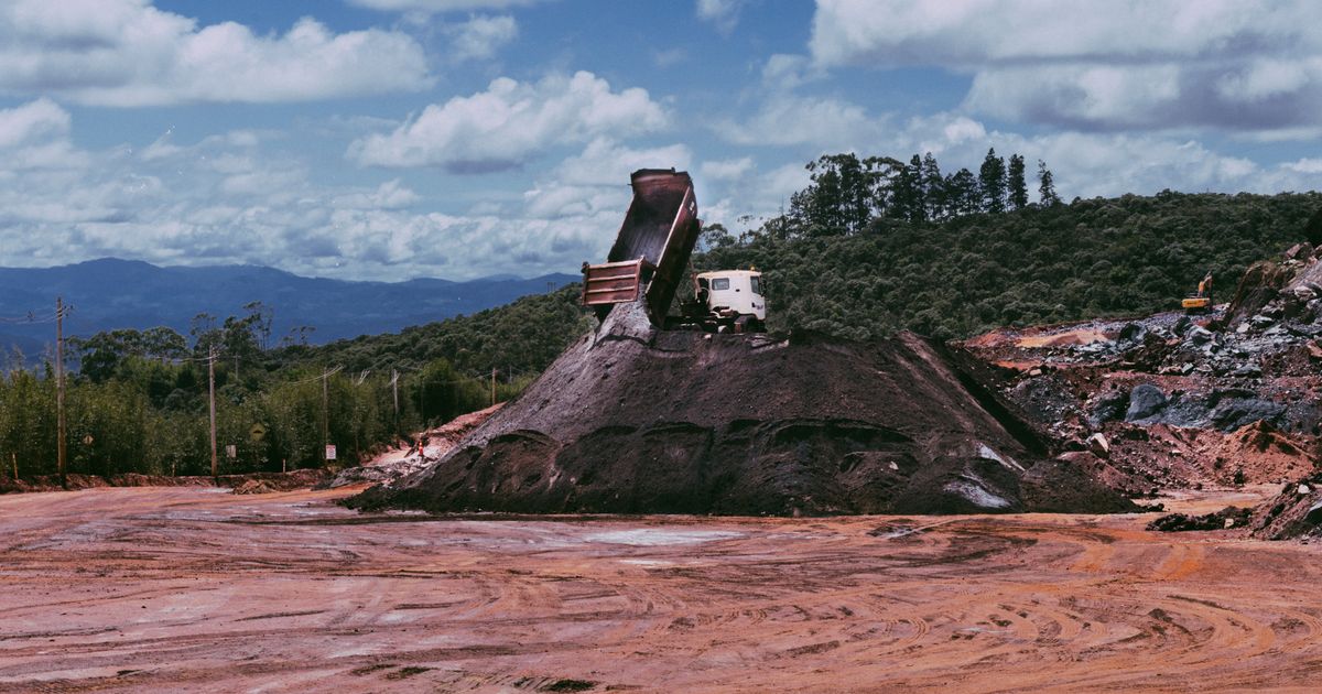Dumper truck offloading soil at an open construction site under a blue sky