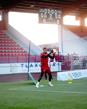 A soccer goalkeeper practices catching during a training session in an empty stadium.