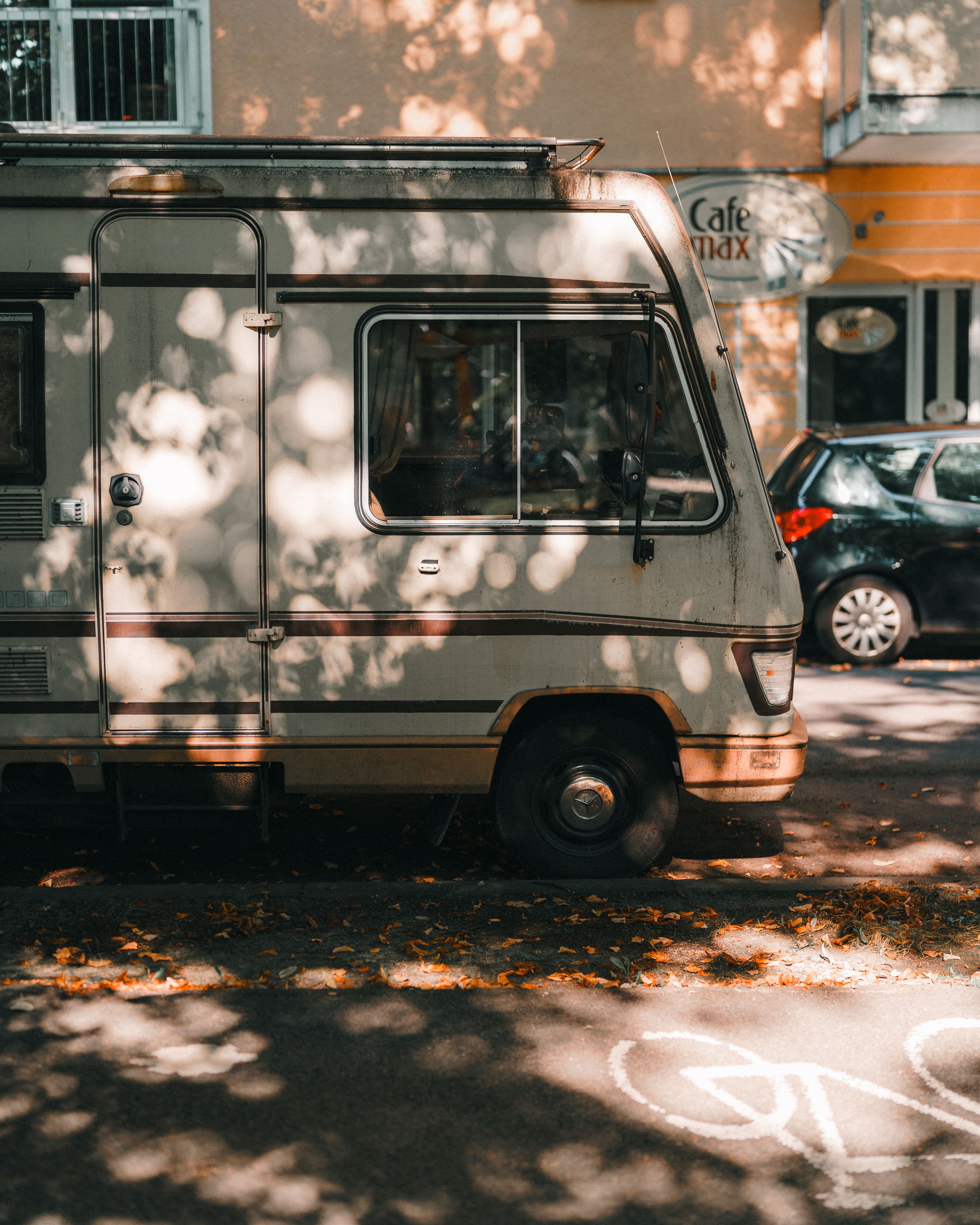 A classic camper van parked on a sunny street, surrounded by dappled light through trees.