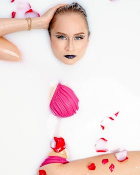 Model in a milk bath with pink swimsuit and rose petals. Artistic beauty concept.