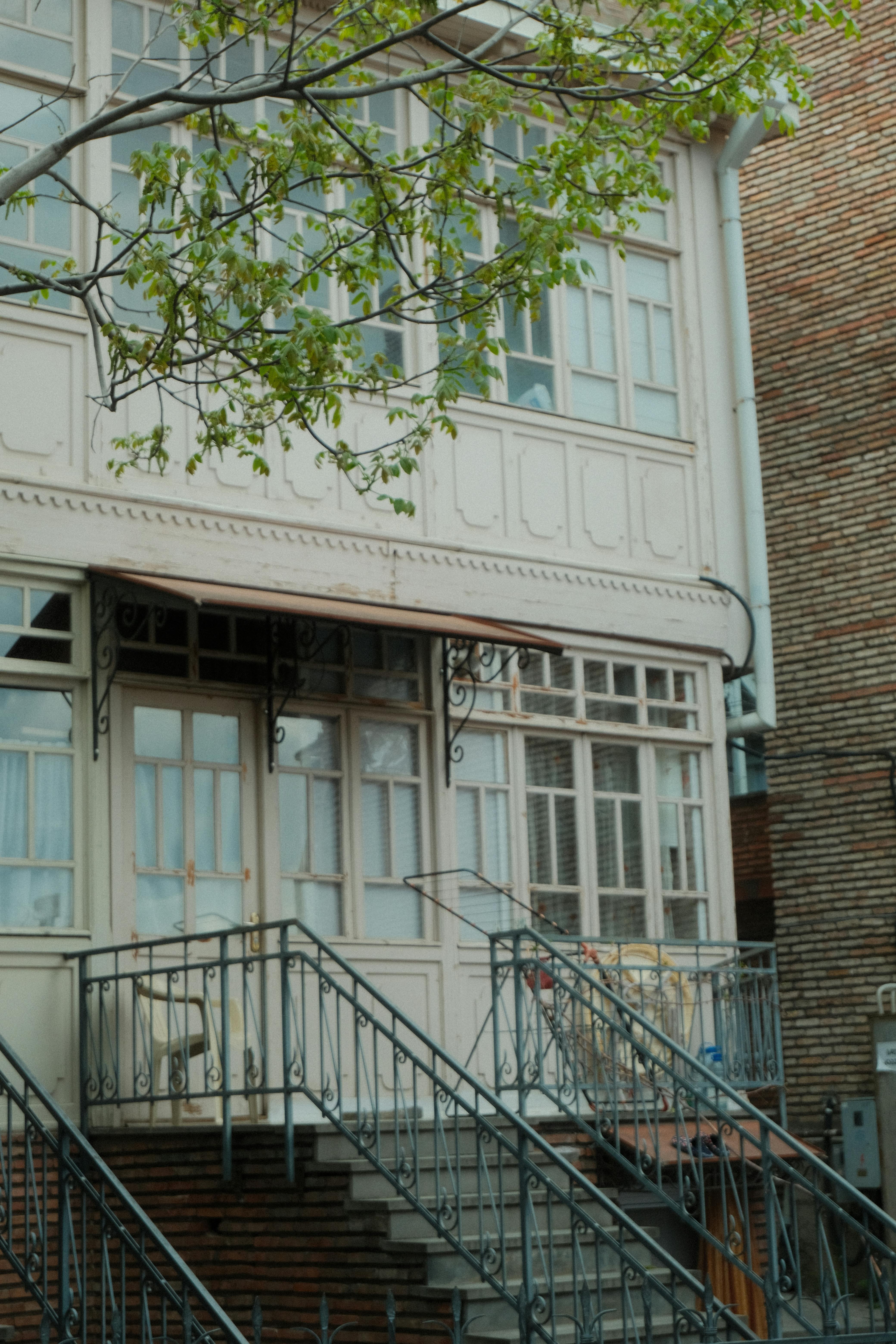 Free Beautiful view of classic Tbilisi wooden balcony with intricate ironwork stairs and lush greenery. Stock Photo