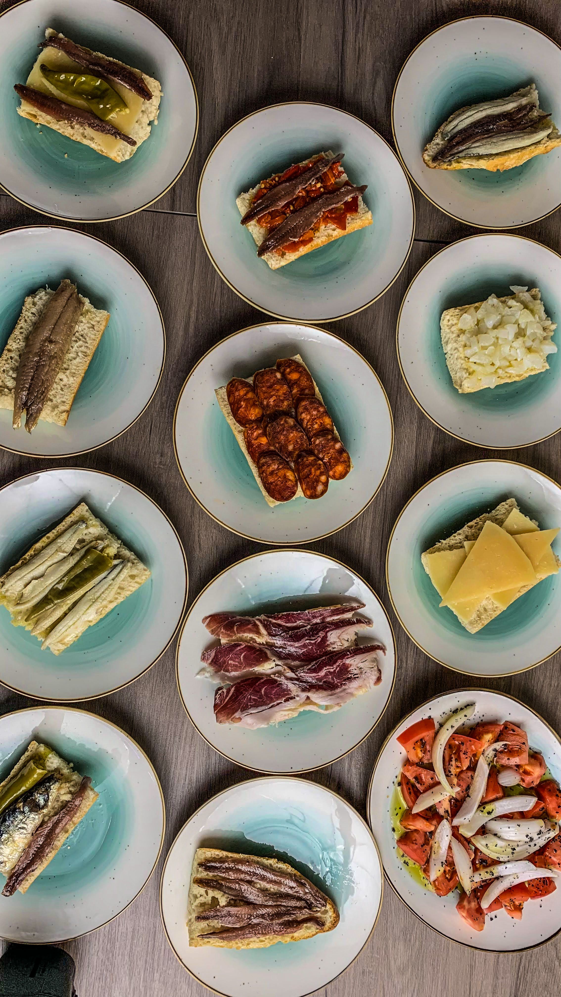 Overhead view of assorted tapas on blue ceramic plates, featuring a variety of cured meats and vegetables.