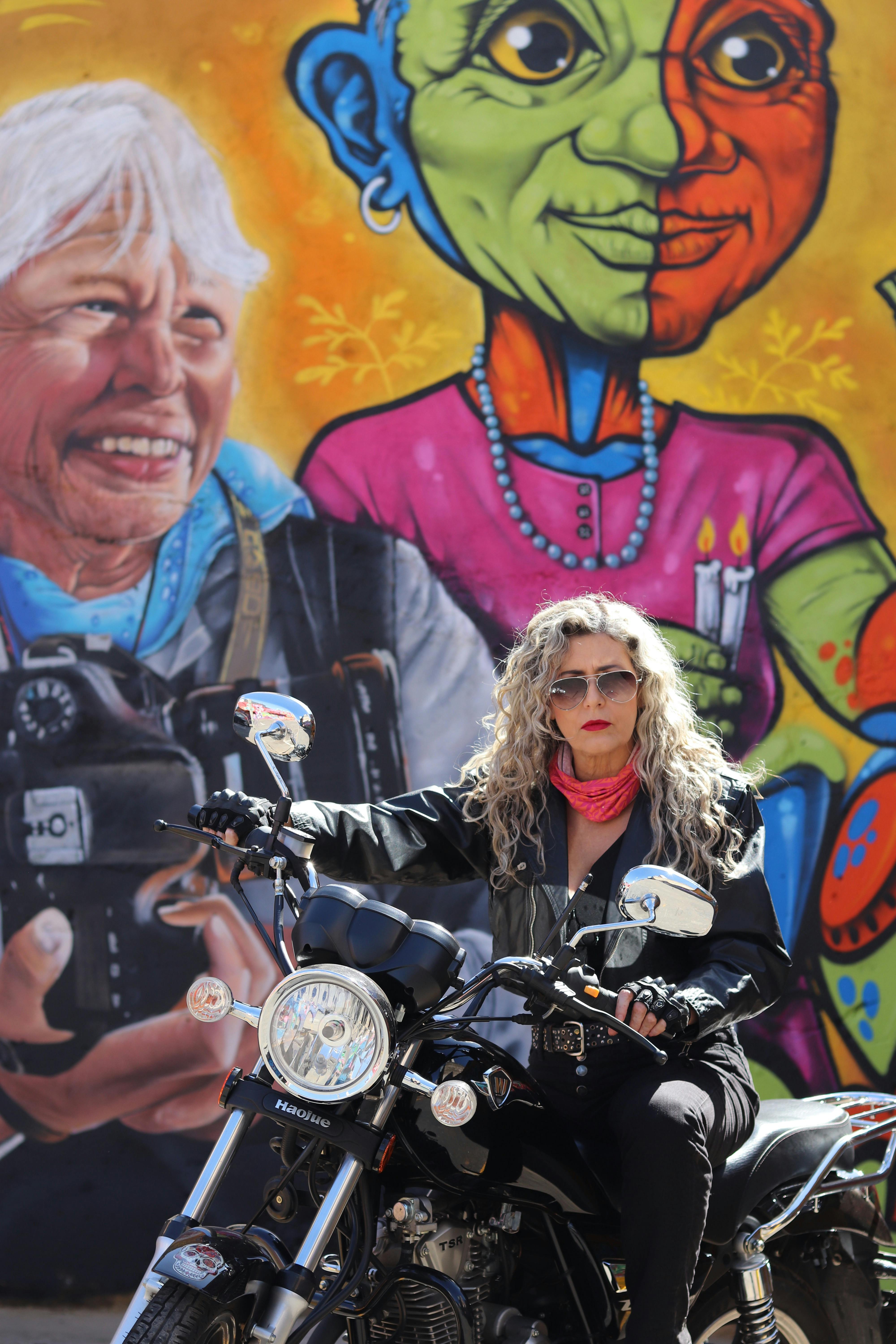 A confident biker poses in front of a colorful mural in Goiânia, Brazil, exuding urban vitality.