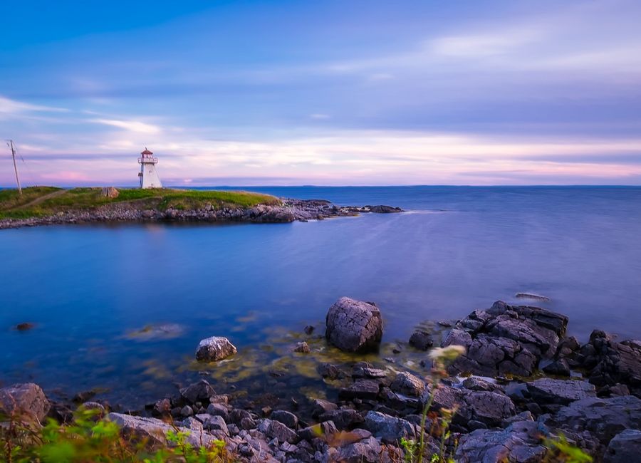 Beautiful view of Cape Auguet Lighthouse during sunset with calm ocean and rocky shore.
