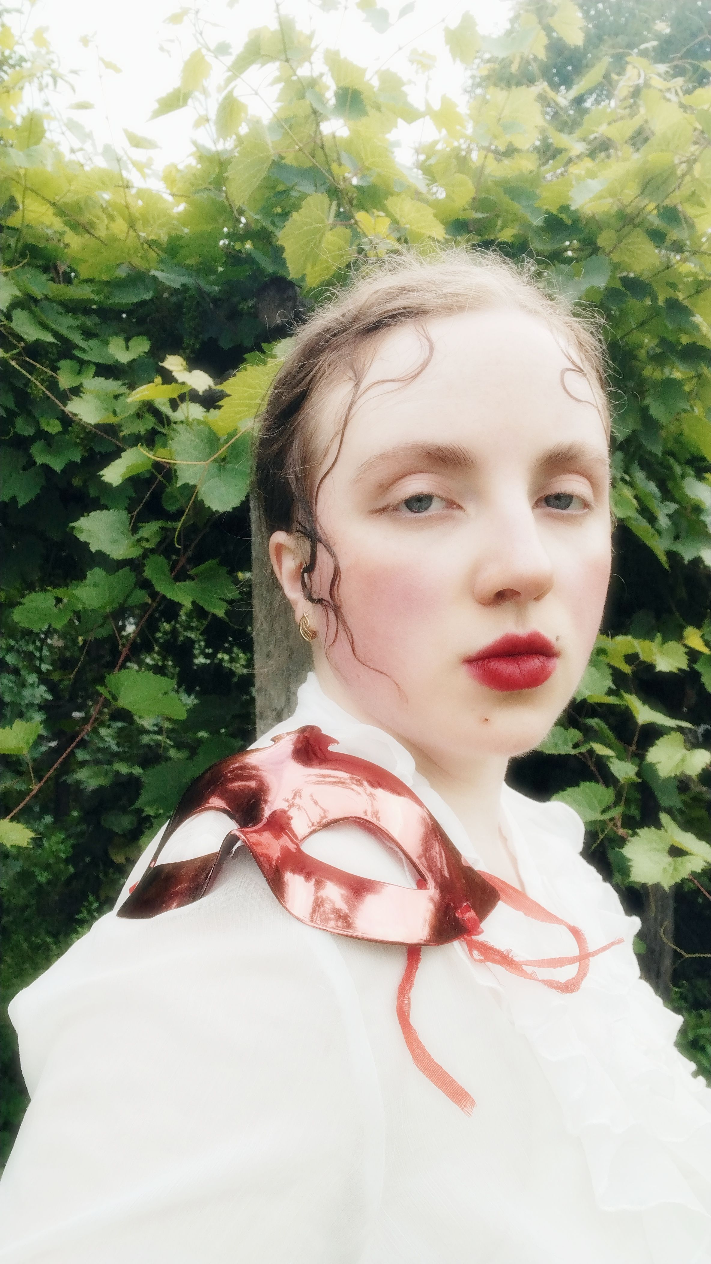 A dreamy portrait of a person with a red mask on a leafy background, evoking a vintage feel.