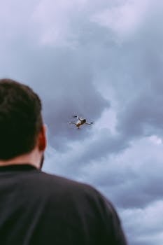Person observing a drone against a dramatic cloudy backdrop, showcasing aerial technology.