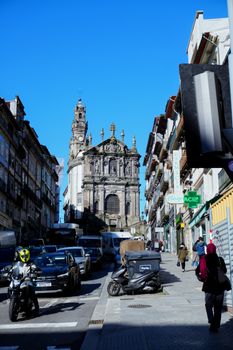 Vibrant city street scene with historic stone church and active pedestrian traffic under a clear sky.