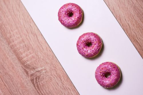 Free Delicious pink frosted doughnuts placed elegantly on a wooden surface. Stock Photo