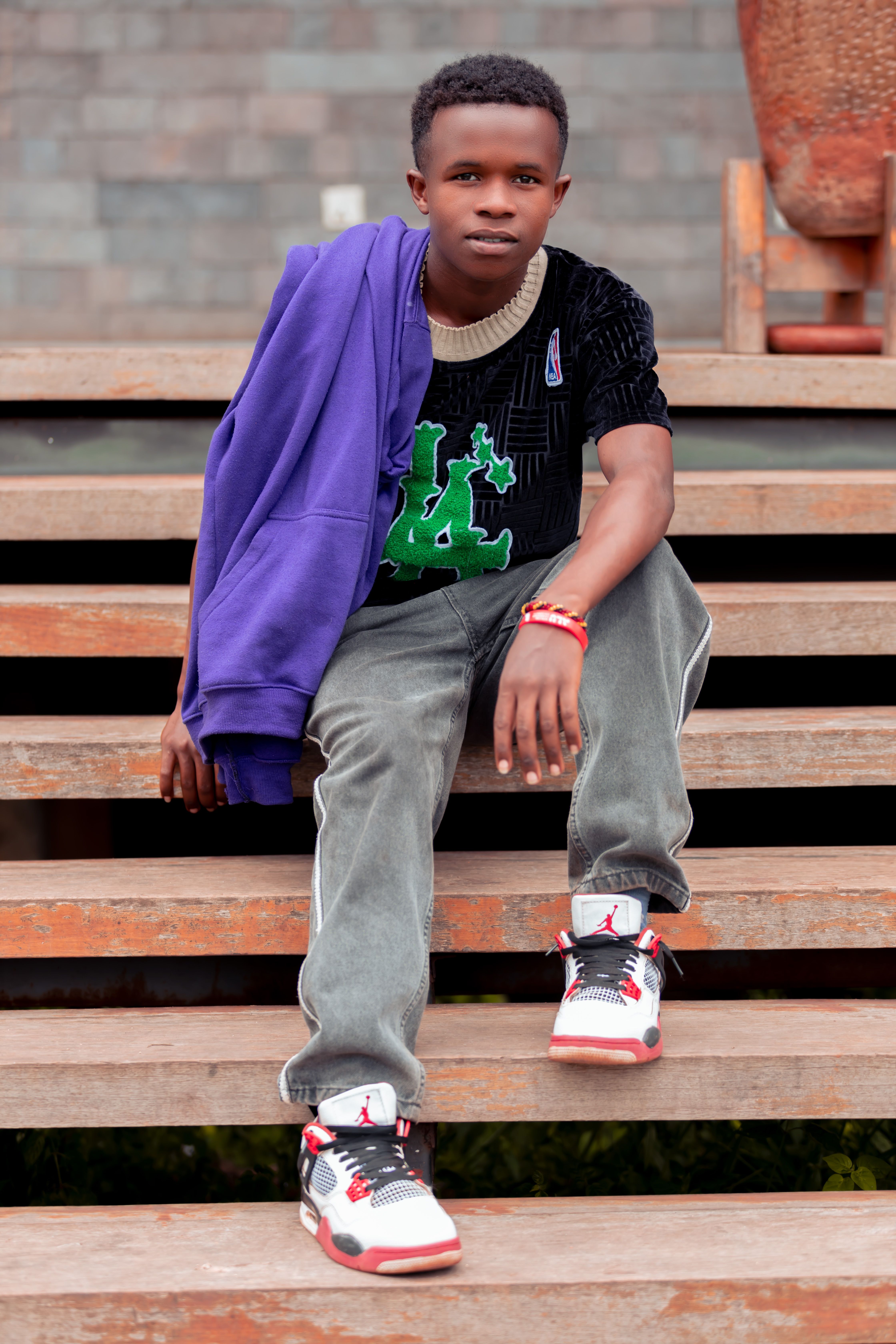 A fashionable teenager sits on outdoor wooden stairs in trendy casual attire, looking confidently at the camera.
