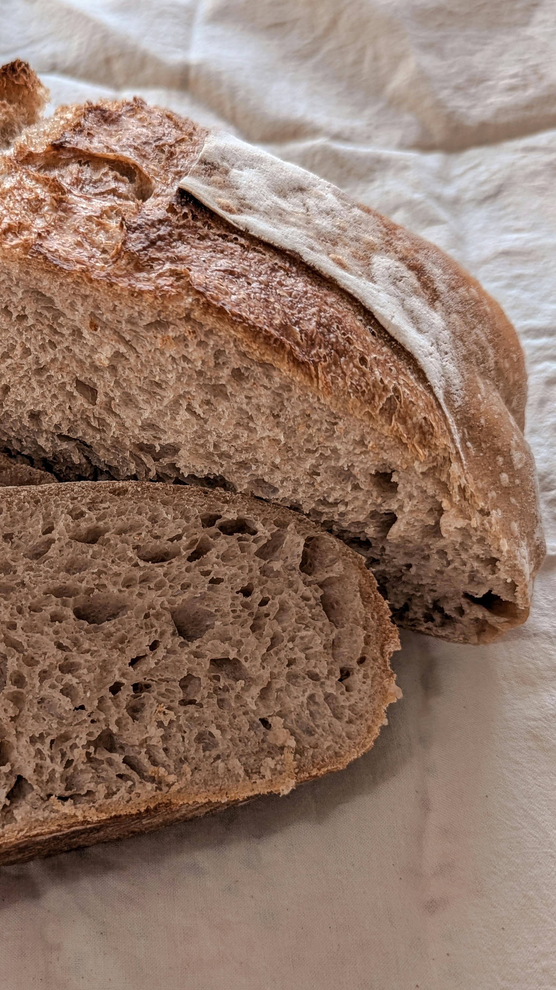 Close-up of sliced artisan sourdough bread on a linen fabric background, showcasing texture.