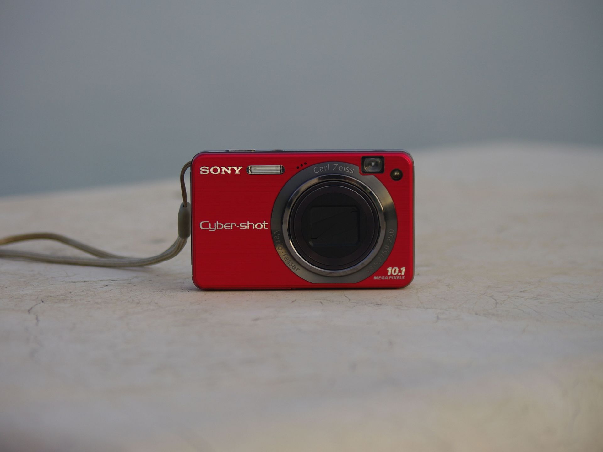 Close-up of a red Sony Cyber-shot digital camera with Carl Zeiss lens on a neutral background.