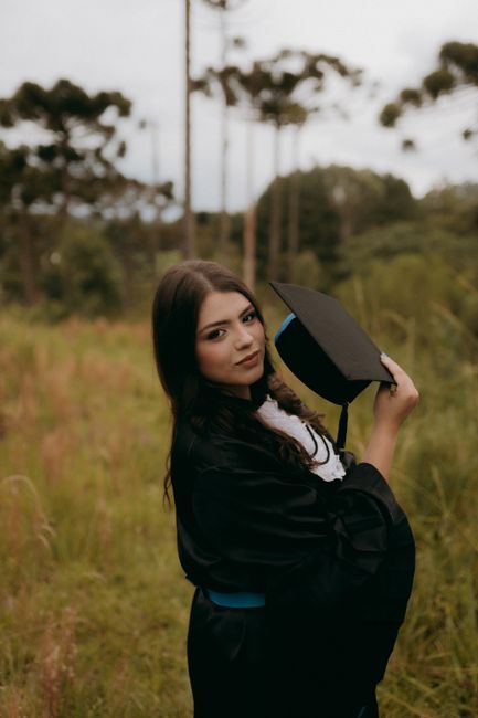 A young woman in a graduation gown celebrates her achievement in a serene outdoor setting.