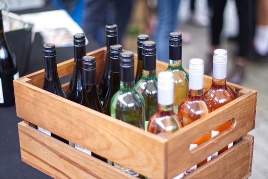 A wooden crate filled with diverse wine bottles at an outdoor gathering.