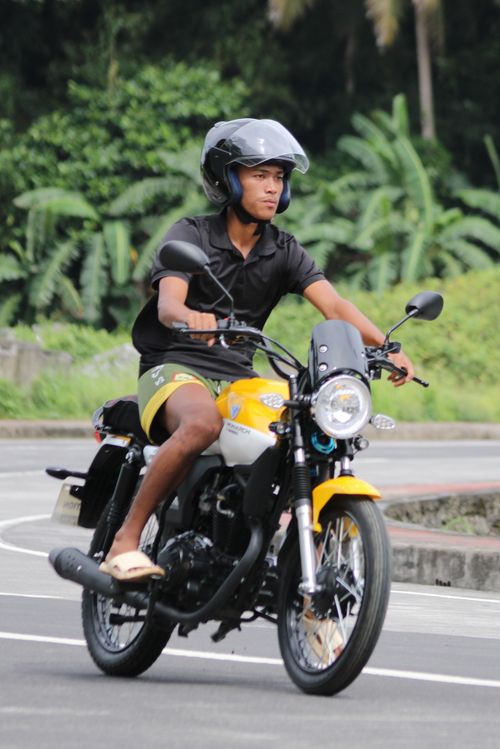Free A young man riding a yellow motorcycle on a scenic outdoor road. Stock Photo