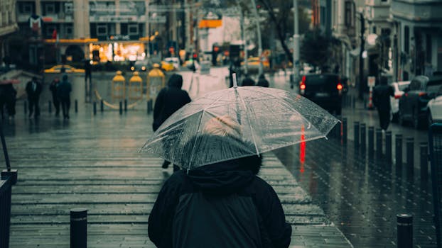 A person walks on a rainy city street under a transparent umbrella.