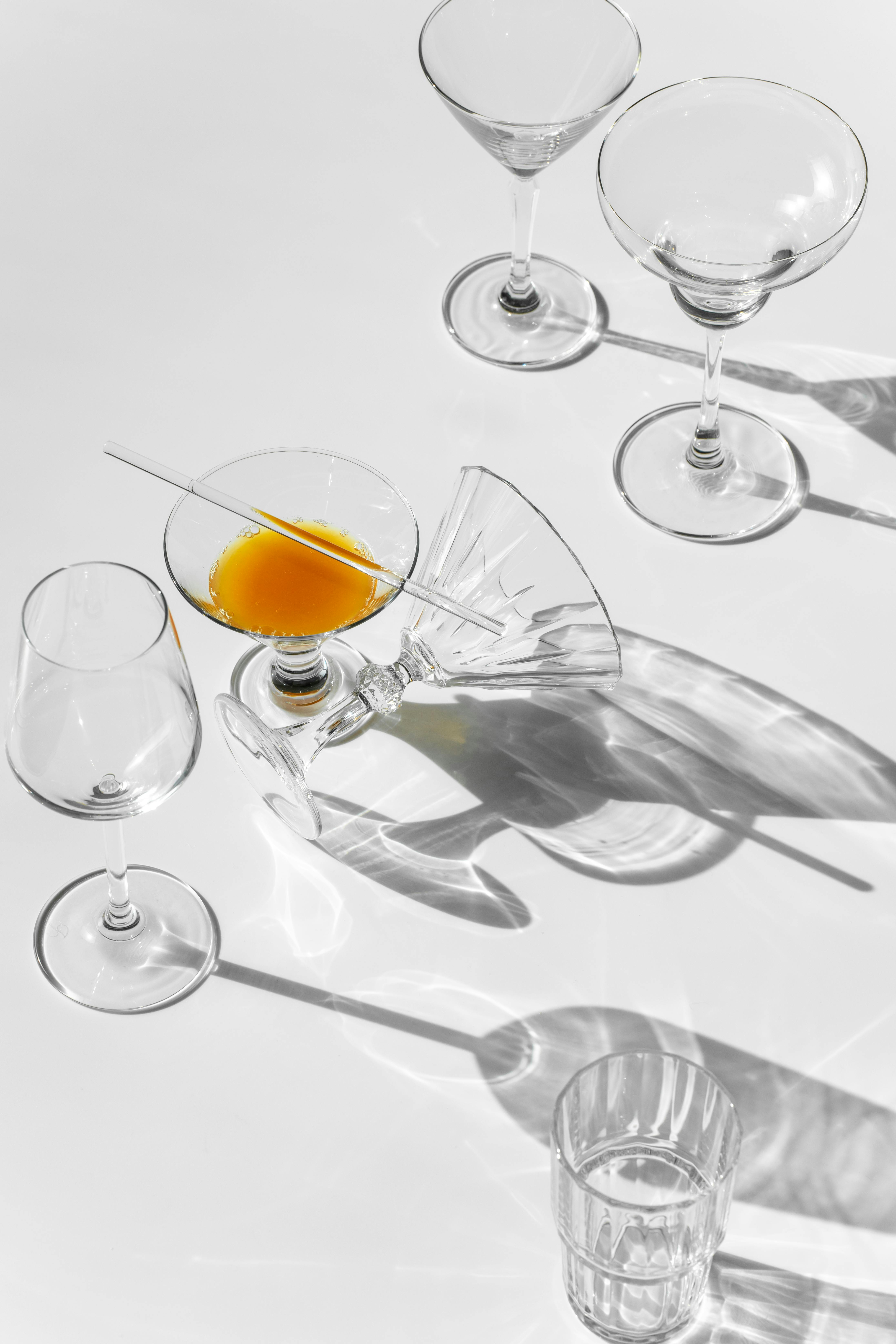 Artistic arrangement of glassware with an orange juice spill casting shadows.