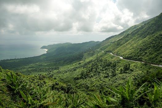 在多云的天空下，俯瞰海岸边郁郁葱葱的绿山，景色壮丽