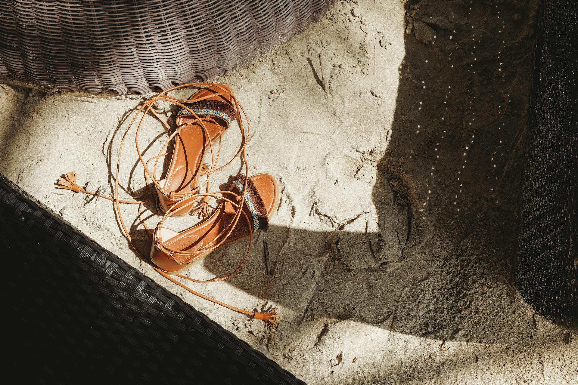 Close-up of brown sandals with tassels on beach sand, captured in sunlight. Perfect for summer vibes.