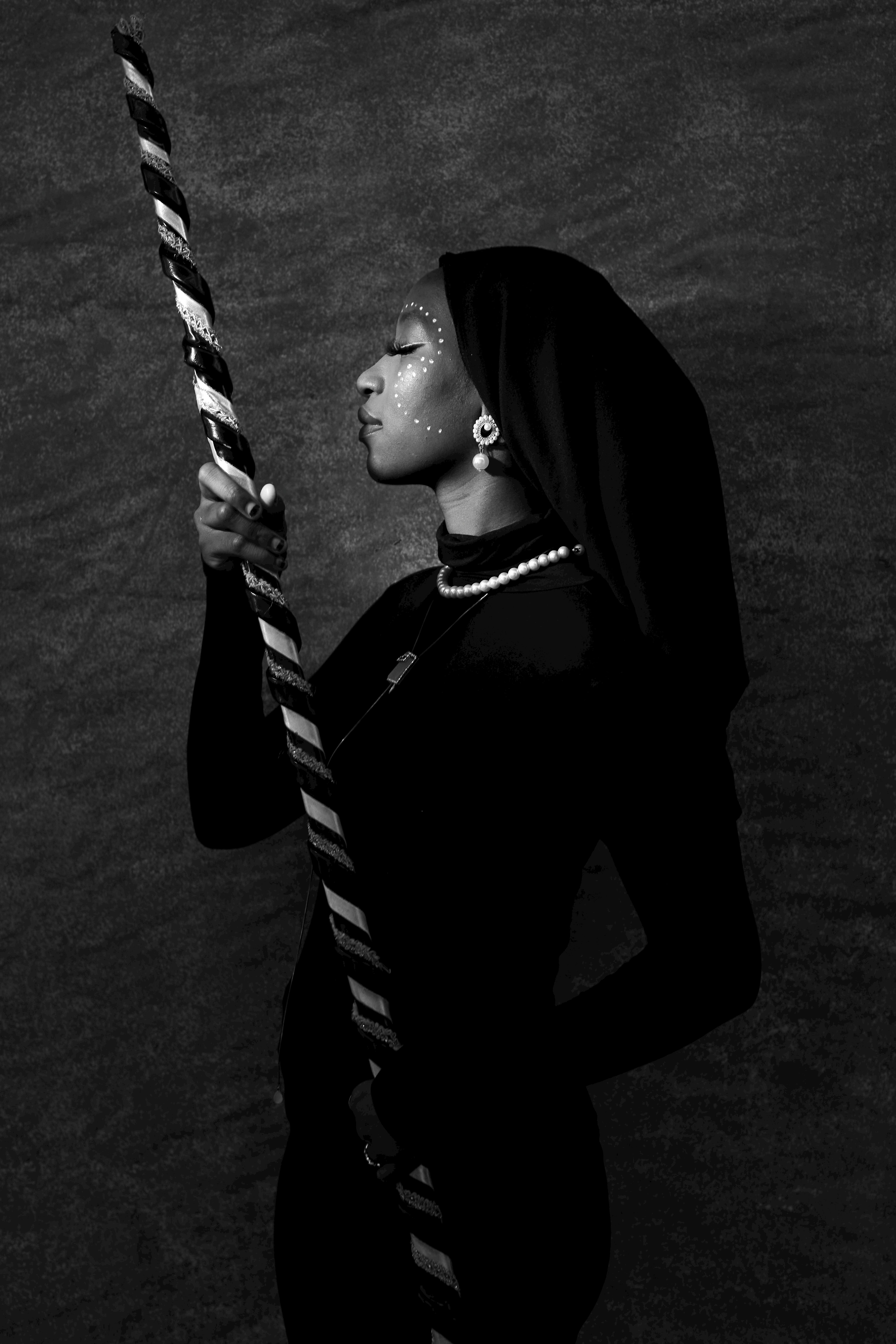 Striking black and white portrait of a Nigerian woman in traditional attire holding a decorative stick.