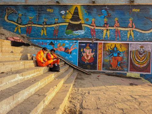 Free Vibrant murals on Varanasi ghats with two people seated, capturing cultural essence. Stock Photo