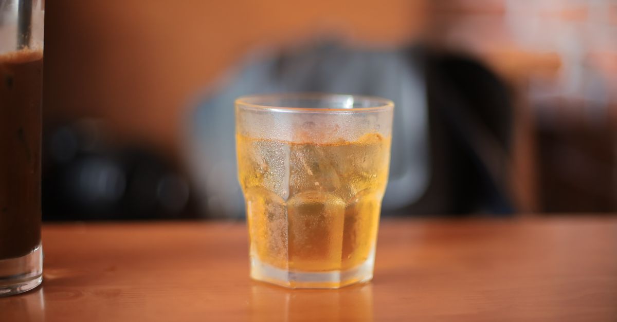 Bebida gelada com cubos de gelo em um copo sobre uma mesa de madeira com fundo de café desfocado.