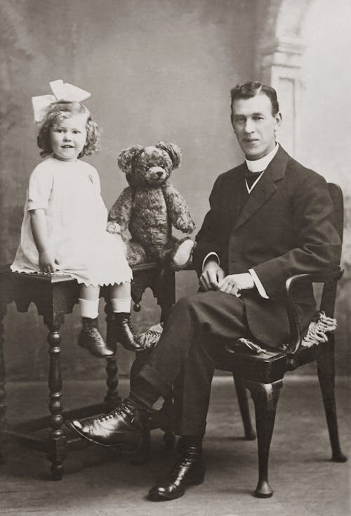 Grayscale Photo of Man With Daughter Sitting On Table Beside A Teady Bear Stuff Toy