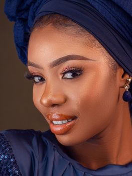 Close-up portrait of a woman with makeup and blue headwrap, exuding elegance and confidence.