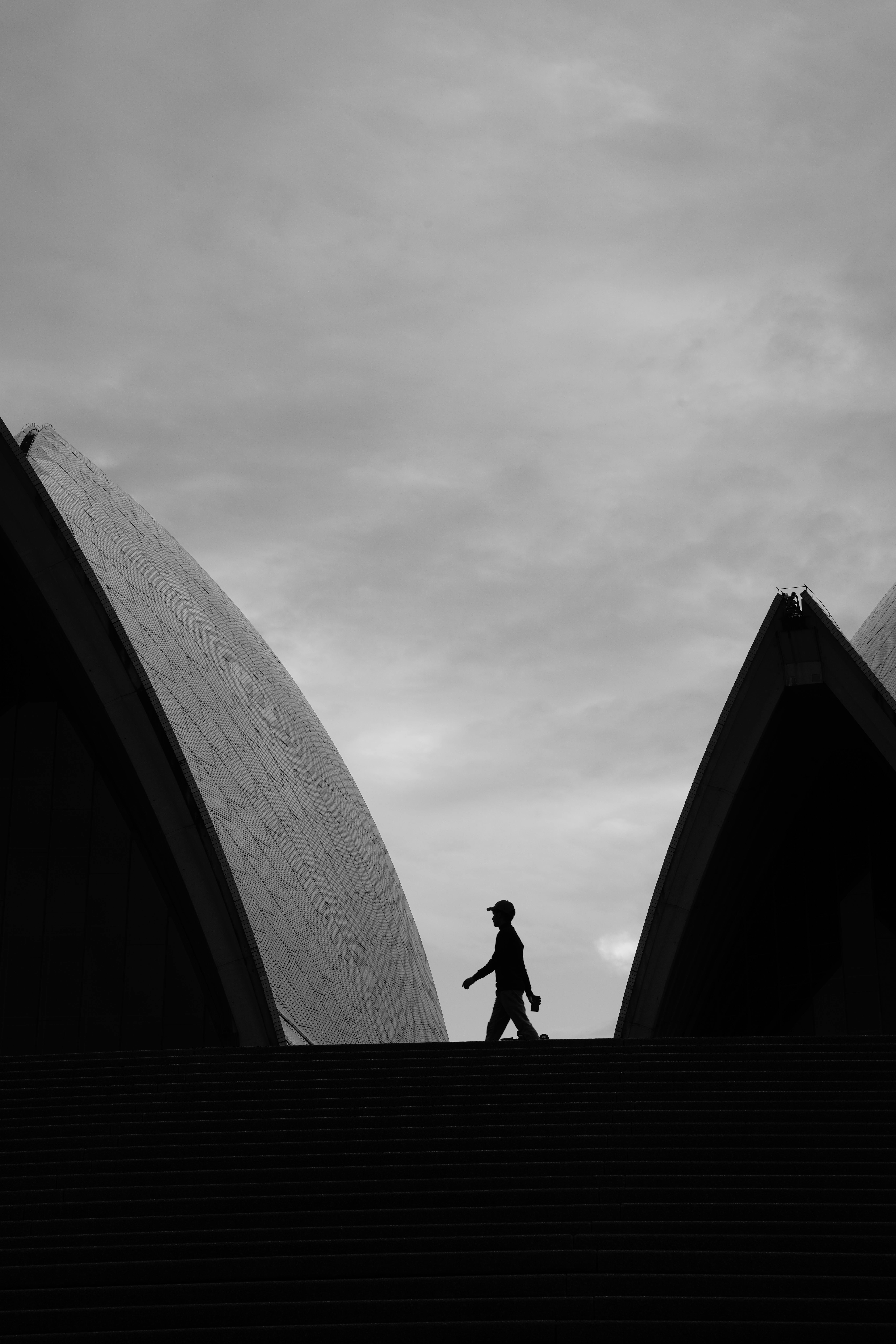 Dramatic black and white silhouette of a person walking at Sydney Opera House.