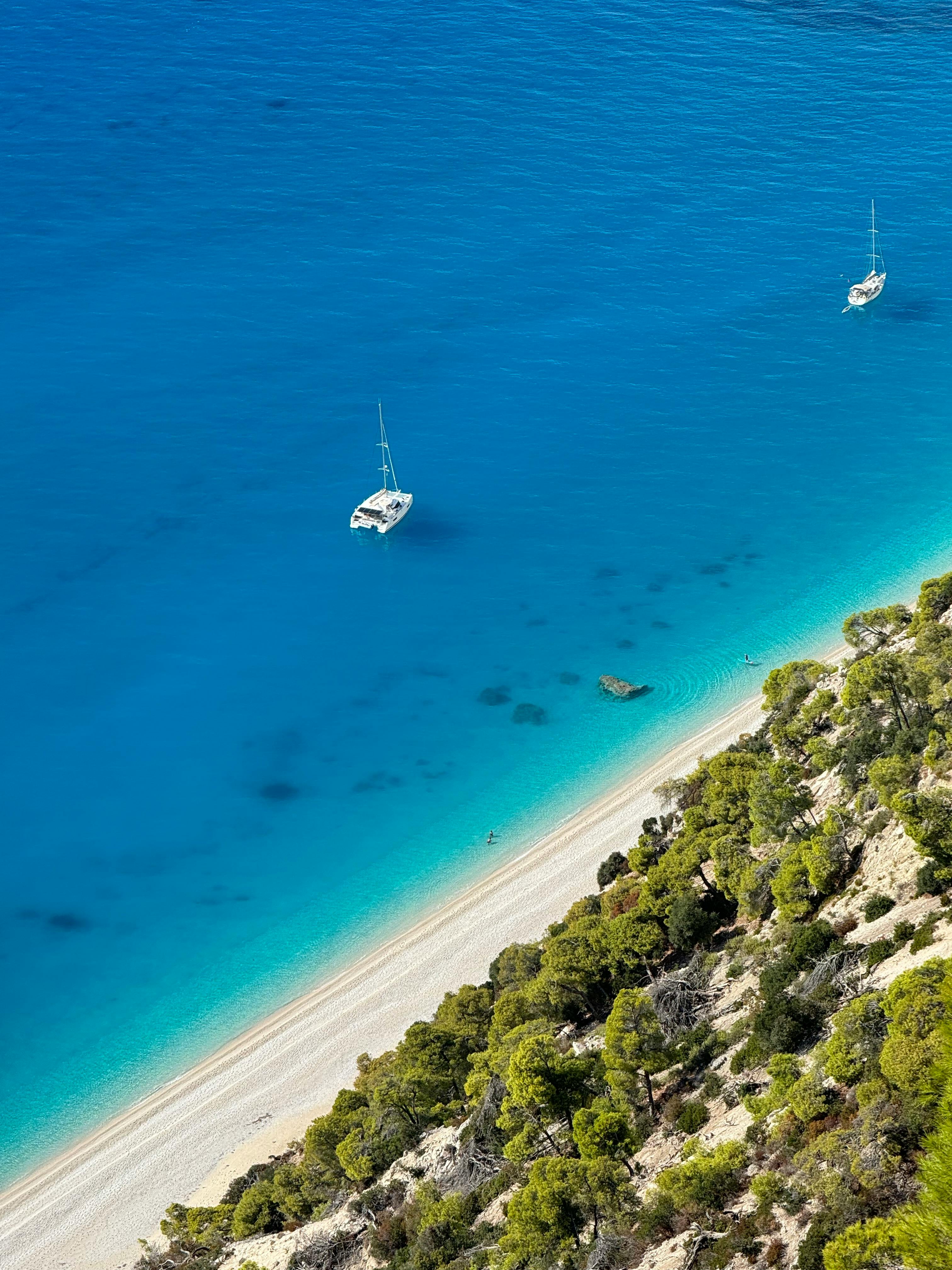 Aerial view of a beautiful Greek beach with turquoise waters and anchored boats.