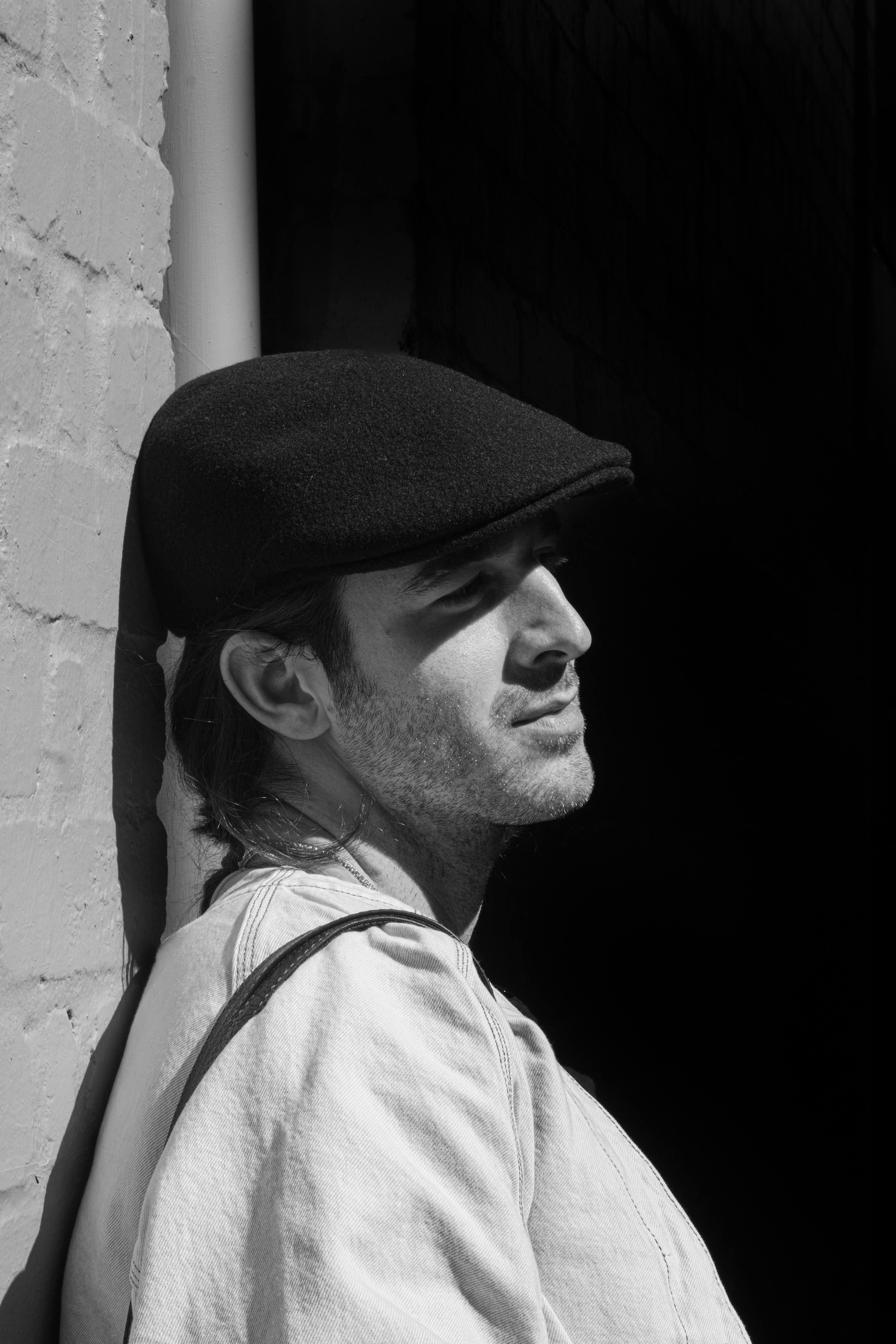 Gratuit Portrait dramatique en noir et blanc d'un homme portant une casquette, appuyé contre un mur au soleil. Photos