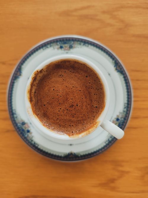 Free Overhead view of a rich coffee cup with frothy top served on a patterned saucer. Stock Photo