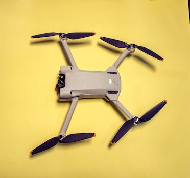 A modern drone with propellers on a vibrant yellow background, viewed from above.