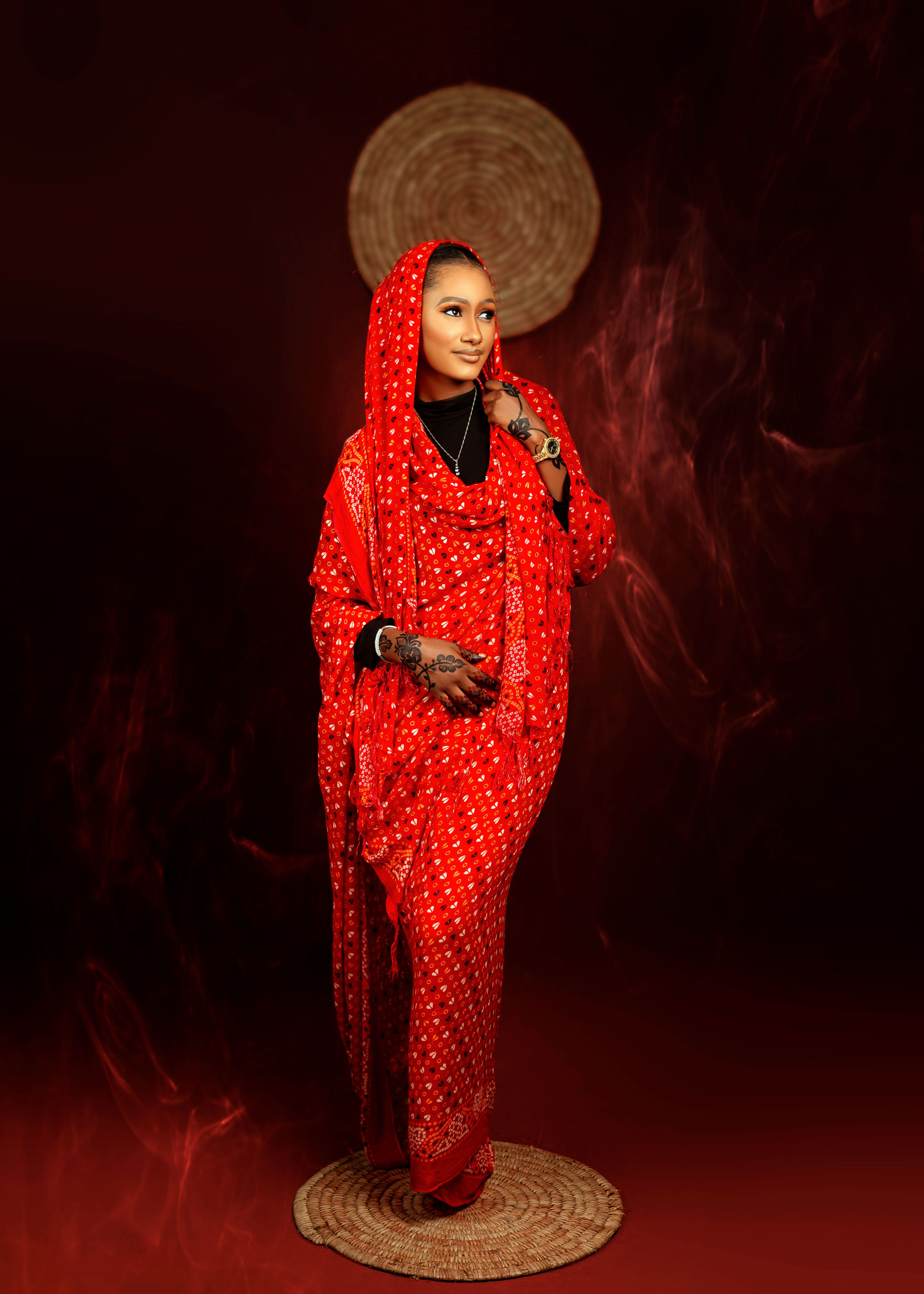 Woman posing gracefully in vibrant red traditional attire against a dark background.