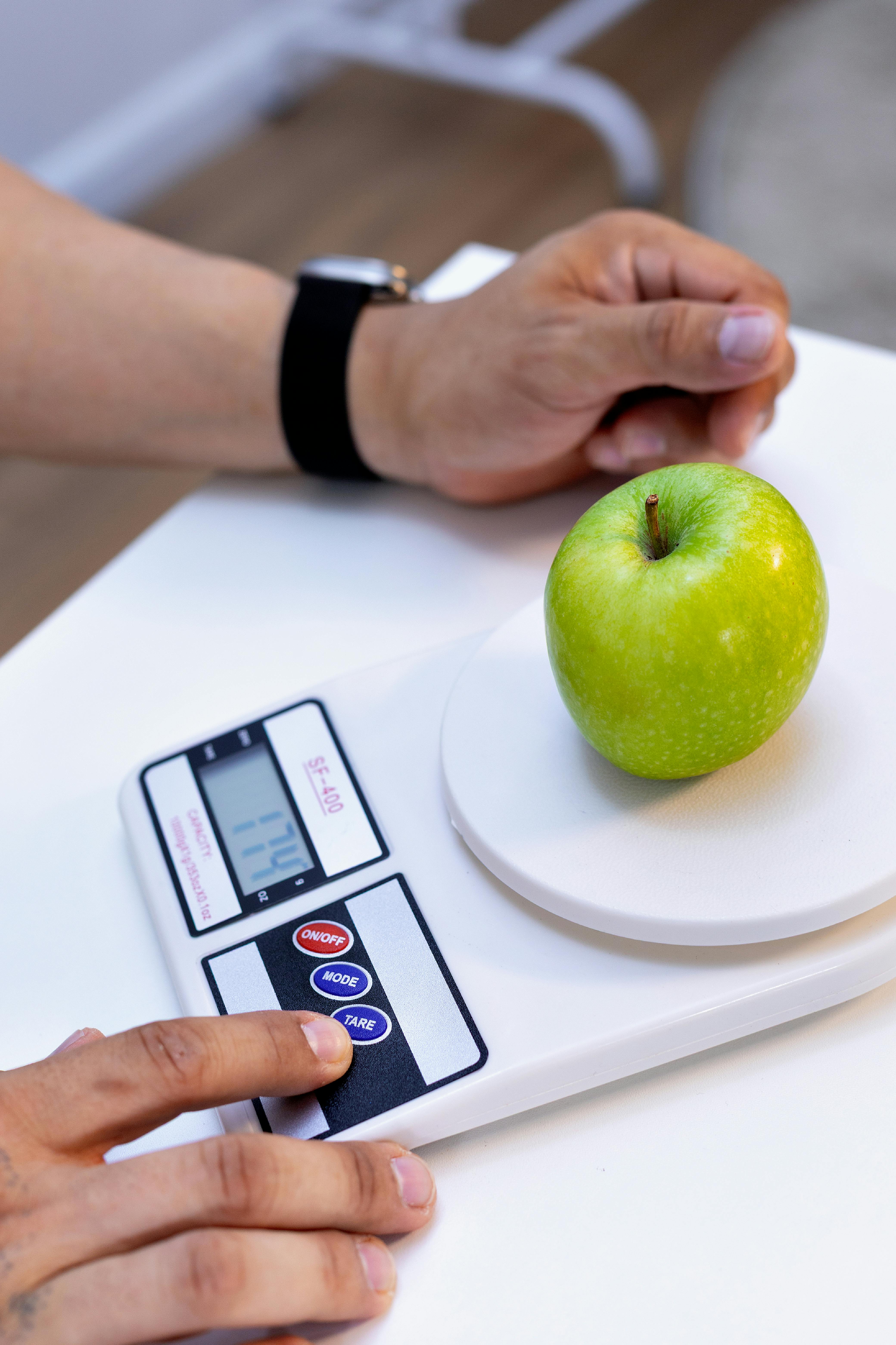 Adult measuring green apple weight on digital scale for healthy nutrition tracking.